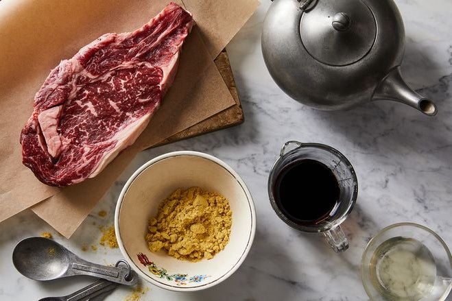 A white and pink piece of raw steak sits on a board, surrounded by an array of ingredients.